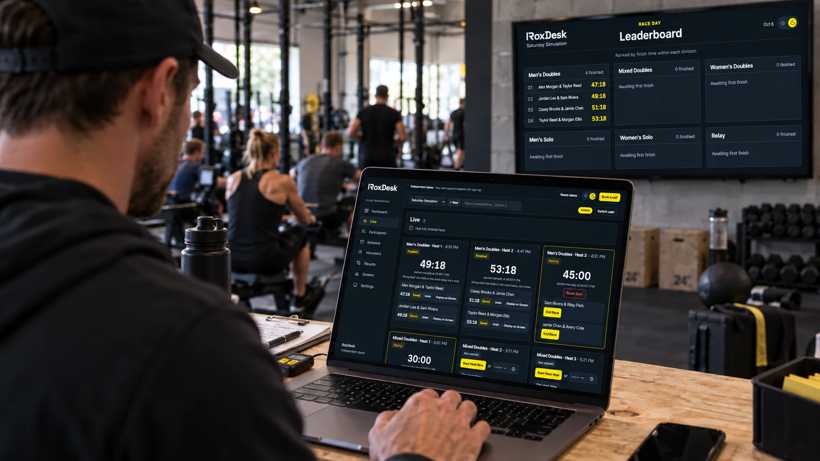 Concept visualization of a gym coordinator using the timing dashboard on a laptop with a leaderboard on the gym wall